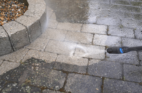 A pressure washer nozzle cleans a stone paver patio, removing dirt and grime from between the stones, demonstrating effective power washing techniques for outdoor surfaces.