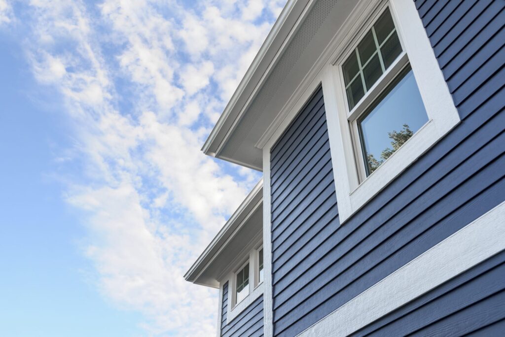 A close-up of a house with deep blue horizontal siding and crisp white trim under a bright blue sky, highlighting the clean, refreshed appearance after professional exterior cleaning in Sylvania, OH.
