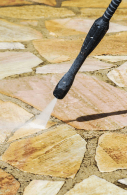 A high-pressure water stream cleans a natural stone patio, revealing fresh, clean surfaces beneath built-up dirt and stains, showcasing the effectiveness of professional power washing services.
