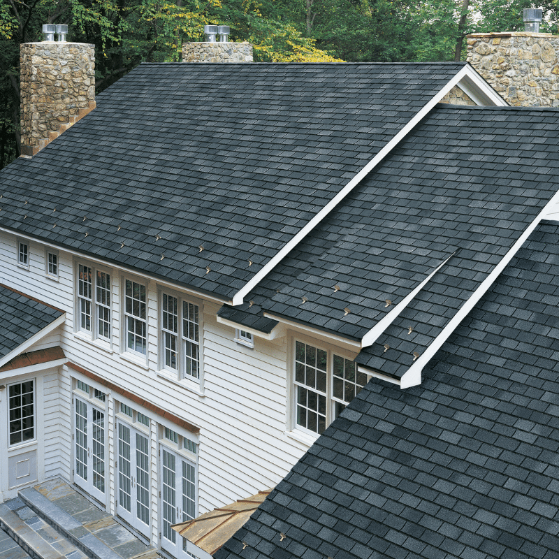 An aerial view of a clean, dark gray asphalt shingle roof on a white-sided home with stone chimneys, showcasing the results of expert roof cleaning in Perrysburg, OH.