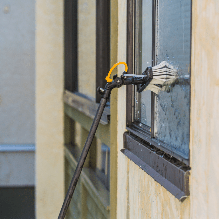 A long-handled window cleaning tool with a brush attachment is used to clean a high-rise window, demonstrating professional window washing services for commercial properties in Toledo, OH.