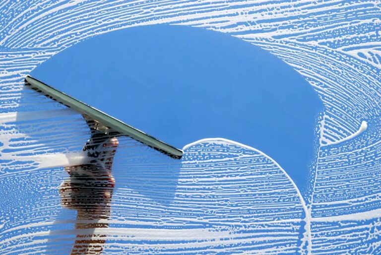 A squeegee gliding across a soapy window, removing streaks and revealing a crisp blue sky reflection, demonstrating the precision and cleanliness of professional window washing services.